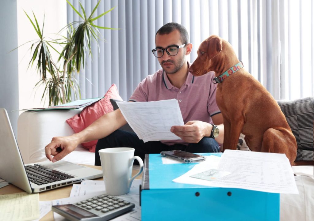 Man calculating monthly costs with dog in front of computer.